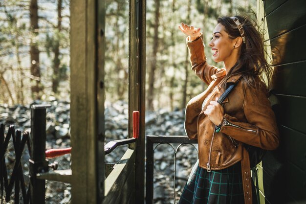 A smiling young woman with a backpack on her back traveling in an adventure by retro train.