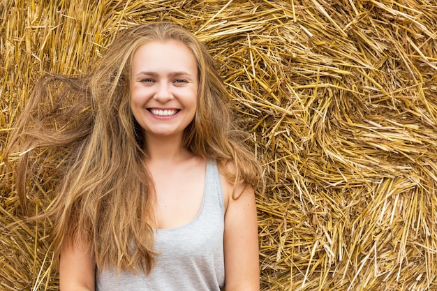 Photo a smiling young woman with a blond with dishevelled hair on the background of hay