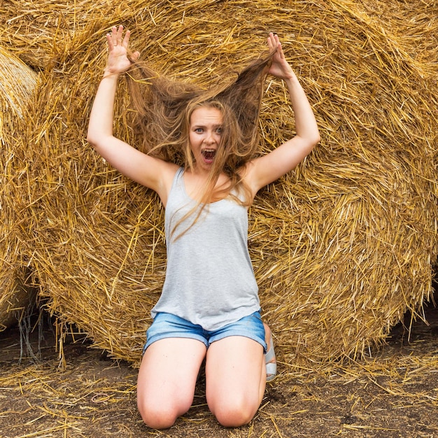 Photo a smiling young woman with a blond with dishevelled hair on the background of hay