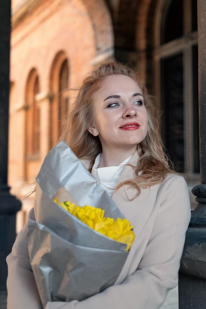 Smiling young woman with bouquet of yellow flowers outdoors Beautiful girl on the date Vertical frame