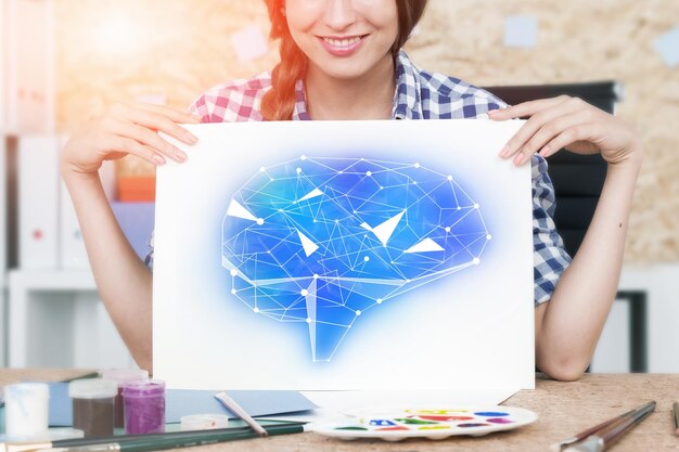 Foto giovane donna sorridente con i capelli intrecciati che tiene un grande foglio bianco di carta con un ologramma cerebrale blu.