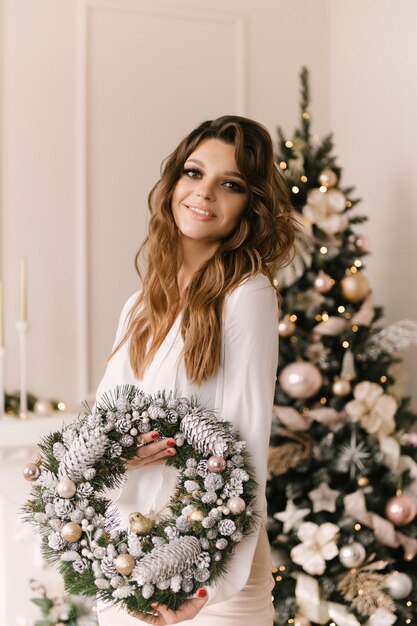 Smiling young woman with a Christmas wreath near the Christmas tree