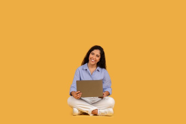 Smiling young woman with curly hair comfortably seated crosslegged on the floor