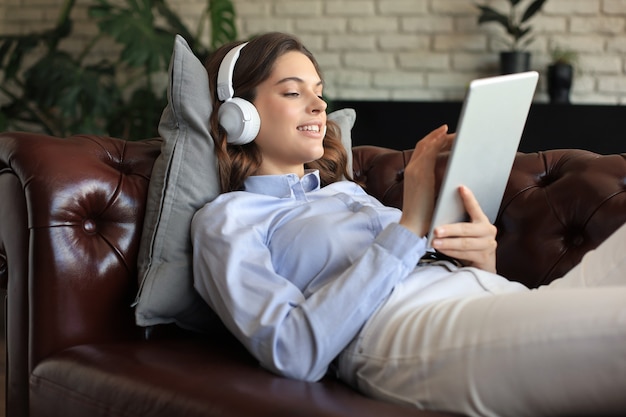 Smiling young woman with headphones and digital tablet on the sofa.