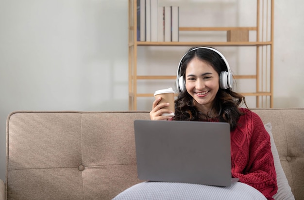 Smiling young woman with headphones using laptop in livingroom\
female studying at home young woman wearing headphones listens\
online web free audio course at home