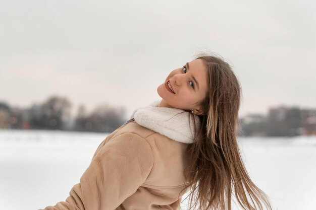 Smiling young woman with long hair enjoys winter nature in beige sheepskin coat Warm womens clothing