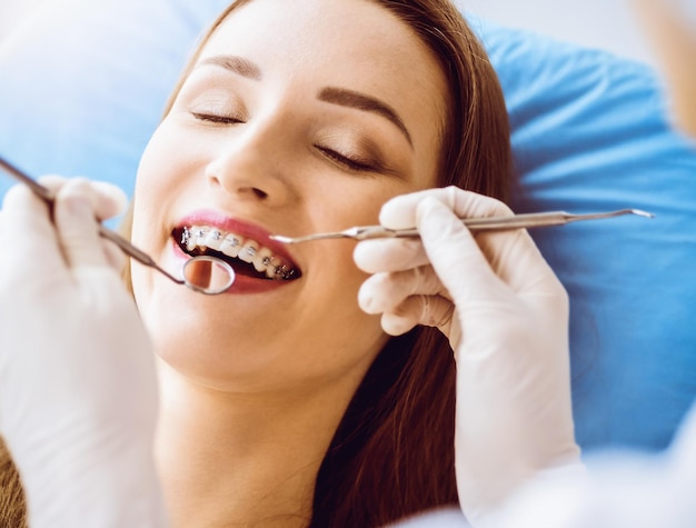 Smiling young woman with orthodontic brackets examined by dentist in sunny dental clinic Healthy teeth and medicine concept