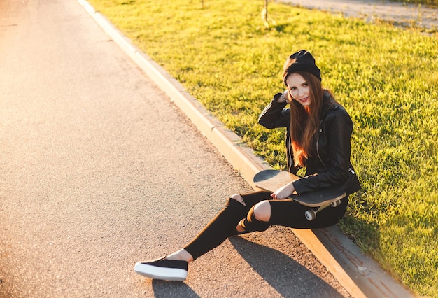 Photo smiling young woman with skateboard sitting at roadside