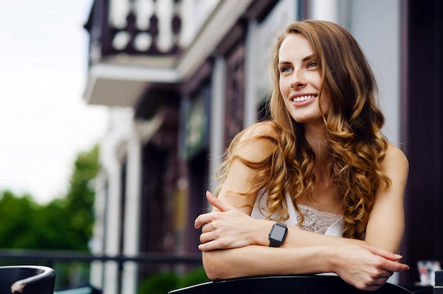 Smiling young woman with smartwatches relaxing and sitting on chair outdoors