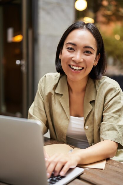 Photo smiling young woman working from cafe or coworking space sitting with laptop studying or doing homew