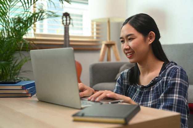 自宅でコンピューターのラップトップで作業している若い女性の笑顔。