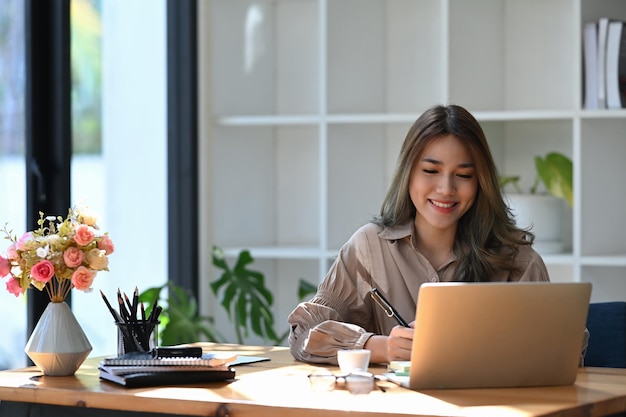 クリエイティブなオフィスでラップトップコンピューターで働く笑顔の若い女性。