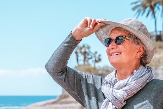 화창한 날과 그녀의 모자를 들고 휴가를 즐기는 바다에서 야외에서 웃는 젊은 할머니