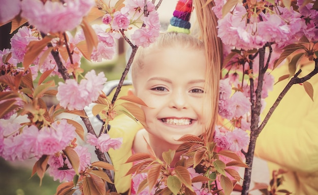 Smilling blonde kid standing in a blooming garden blooming cherry portrait of beautiful little girl