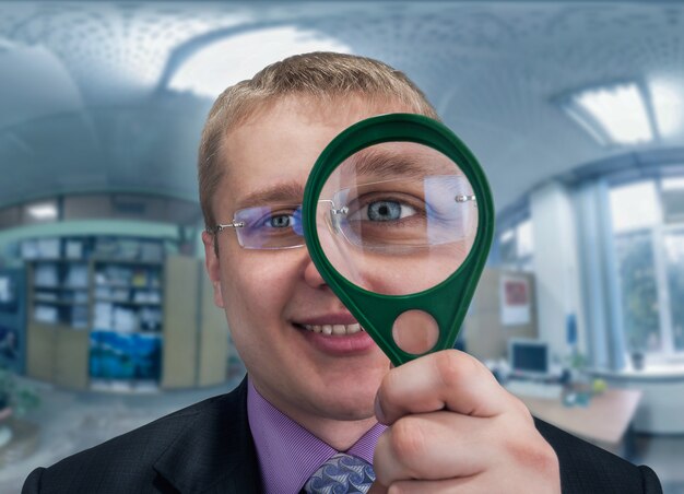 Smilling businessman looks at you through magnifying glass