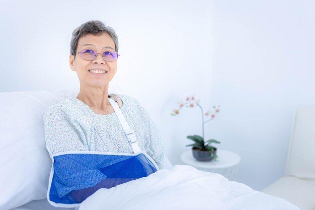 Smilling elderly woman wear arm splint for treatment at hospital Medical treatment health insurance concept