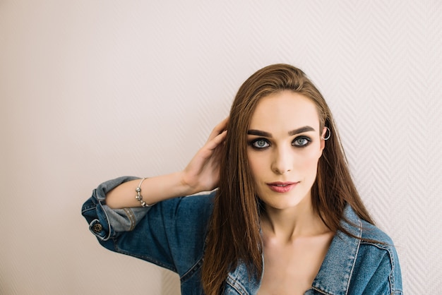 Smilling girl with piercing wearing denim jacket looking at camera, smoky eyes, perfect skin tone