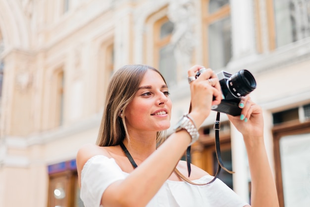 Smilling schoonheid vrouw met retro camera in haar handen tijdens het nemen van foto's op stedelijke oude architectuur. Ontdek nieuwe plekken.