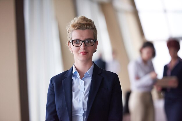 Smilling young business woman in front her team blured in background. Group of young business people. Modern bright  startup office interior.