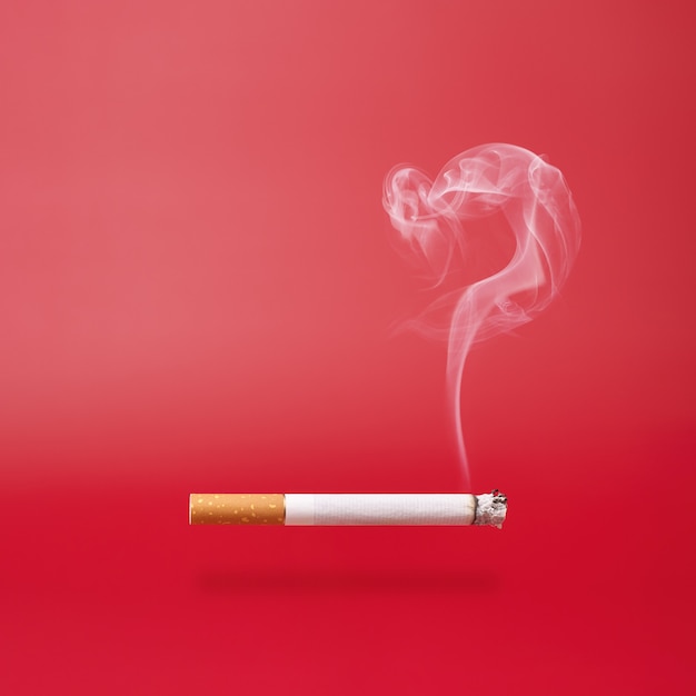 Smoke as question mark and a smoking cigarette on red background with copy space.