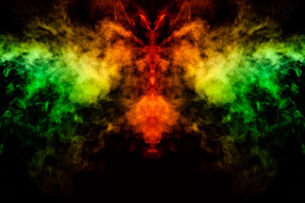 Smoke of different green yellow orange and red colors in the form of horror in the shape of the head face and eye with wings on a black isolated background Soul and ghost in mystical symbol