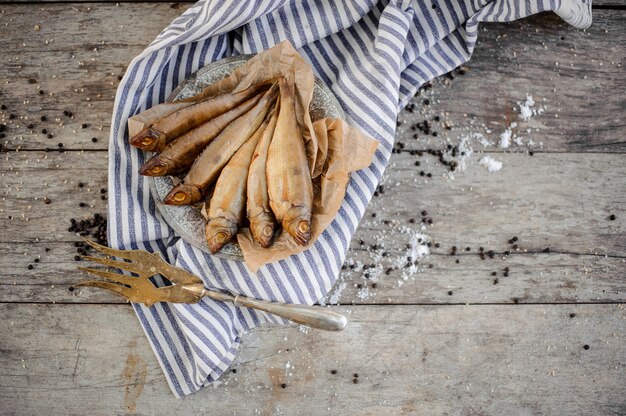 Smoke-dried fish on the metal plate on a baking paper on the grey striped napkin on the wooden table.