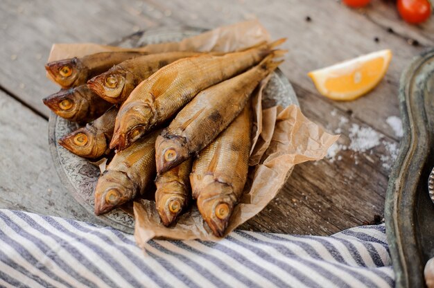 Smoke-dried fish on plate on a baking paper on the grey striped napkin with a salt and lemon on the wooden table.