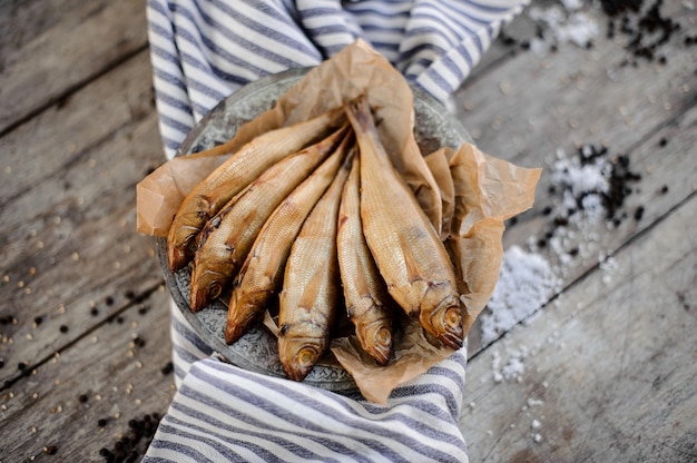 Smoke-dried fish on plate on a baking paper on the grey striped napkin on the wooden table