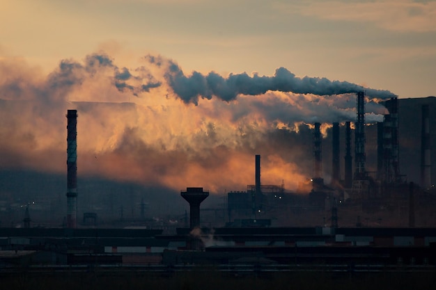 Smoke emitting from factory against sky at sunset