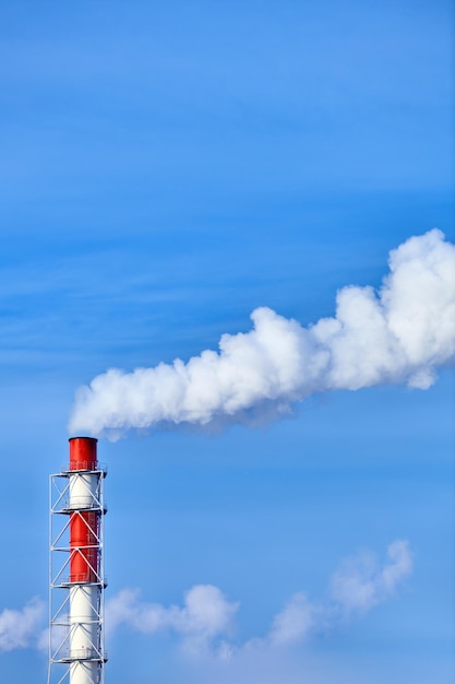 Smoke exhausting from chimney. Huge smoke from the pipe. Red-white chimney of factory. Environmental pollution. Carbon dioxide emissions. Global climate protection concept.