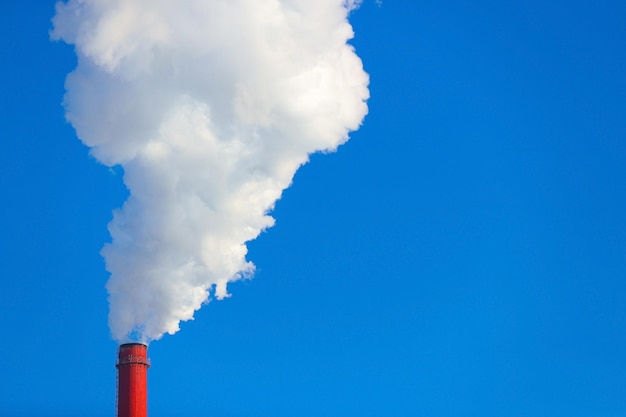 Photo smoke is coming from a red chimney against a blue sky