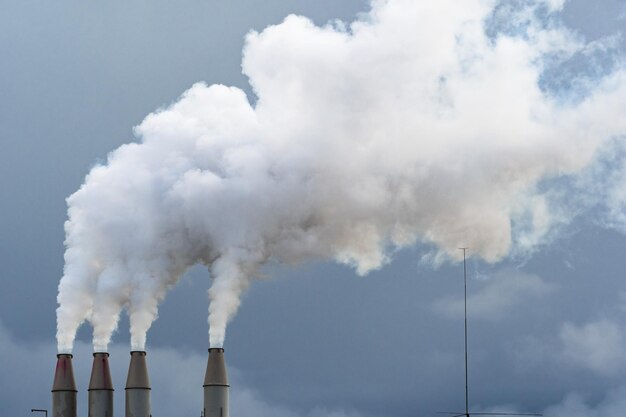 Smoke and steam rising into the air from power plant stacks dark clouds background concept for environmental pollution and climate change