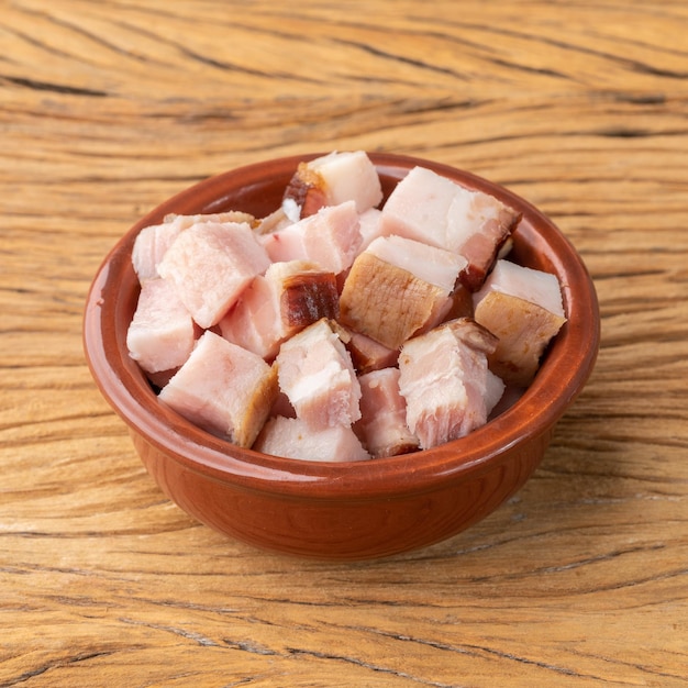 Smoked bacon cubes in a bowl over wooden board.