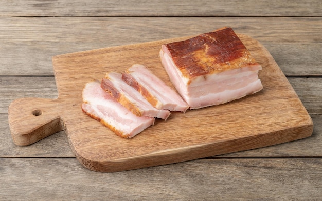 Pancetta affumicata con fette e coltello su tavola di legno.