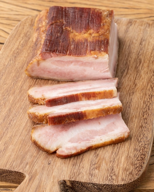 Smoked bacon with slices over wooden board.