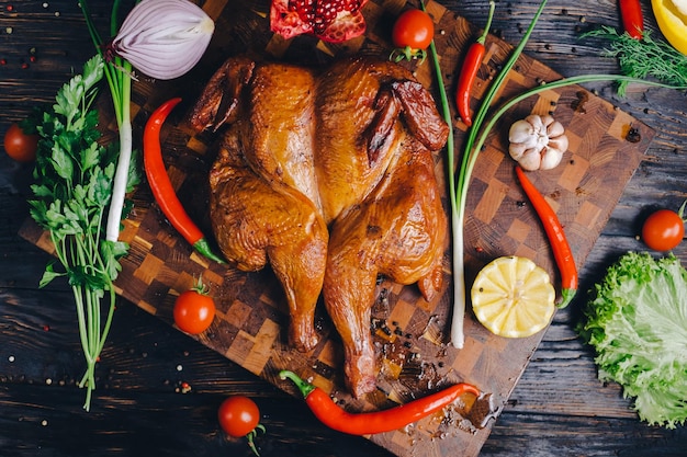 smoked chicken chicken baked in a smokehouse on a cutting board decorated with vegetables pepper chili pepper lemon rosemary onion