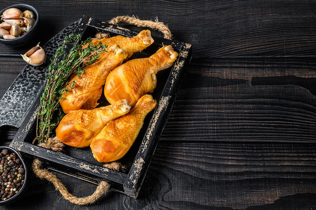 Smoked chicken leg drumsticks with herbs and spices. Black wooden background. Top view. Copy space.