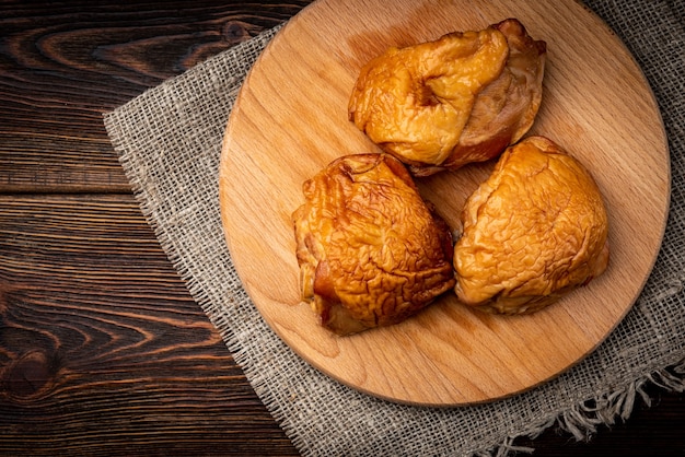 Smoked chicken thigh on wooden board on dark wooden background.