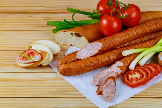 Smoked european sausage on a wooden table with tomato, bread and chives