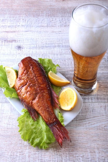 Smoked fish and lemon on green lettuce leaves on Wooden cutting board and glass with beer on white