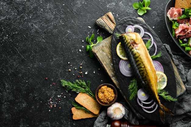 Smoked fish mackerel with onion and lemon on a black plate Top view Free space for your text Rustic style