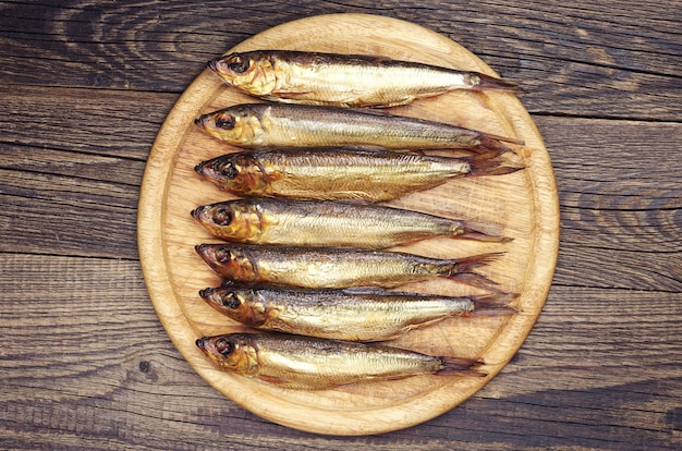 Smoked fish on a round cutting board on wooden table. Top view