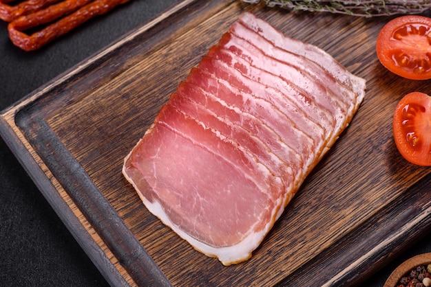 Smoked ham on a dark concrete table with addition of fresh aromatic herbs and spices natural product from organic farm