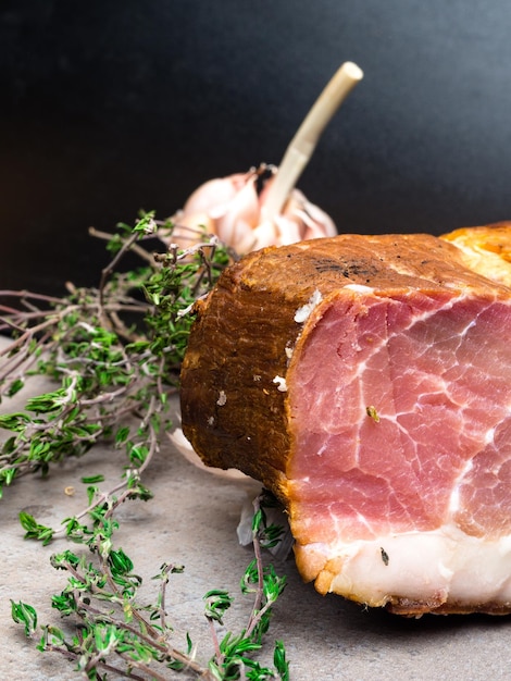 Smoked ham on a stone table with addition of fresh aromatic herbs and spices Natural product from organic farm produced by traditional methods