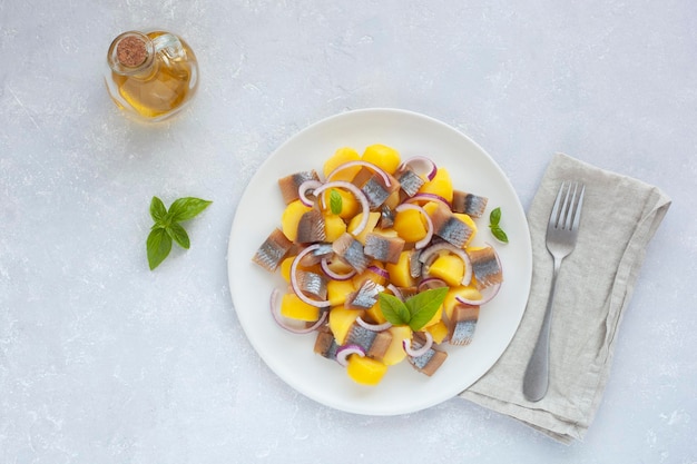 Smoked hering, potatoes and onions salad decorated with basil leaves, olive oil sauce, top view