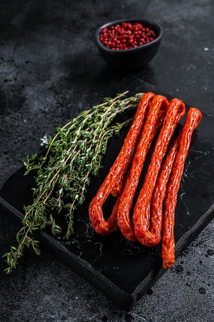 Smoked kabanos sausages with herbs on marble board Black background Top view