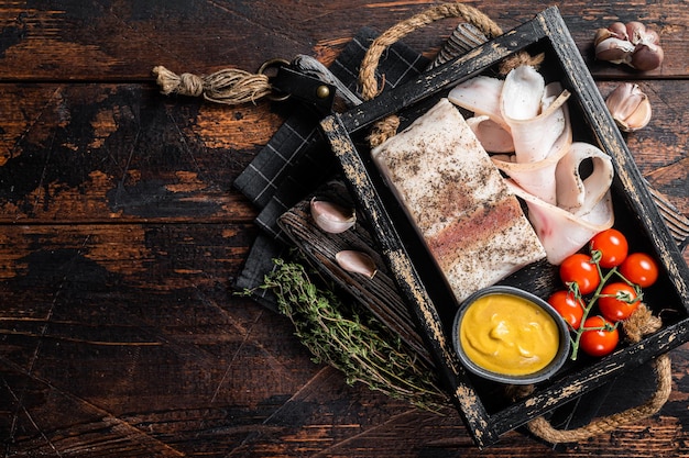 Smoked lard slices with salt garlic and pepper in wooden tray with herbs Wooden background Top view Copy space