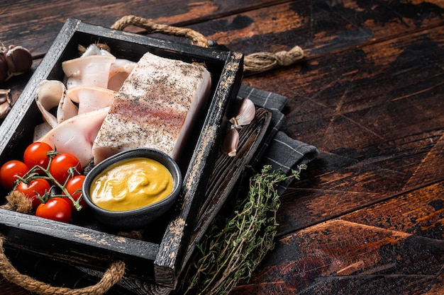 Smoked lard slices with salt garlic and pepper in wooden tray with herbs Wooden background Top view Copy space