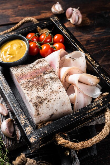 Smoked lard slices with salt garlic and pepper in wooden tray with herbs Wooden background Top view