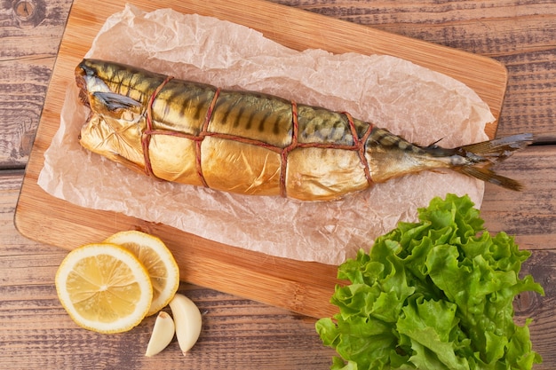 Smoked mackerel fish with lemon and greens on wooden board top view close up